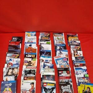 May include: A collection of video game cases, featuring titles for various consoles like PlayStation 2, Wii, and Xbox 360. Games include "Sonic," "Guitar Hero," "Lego Batman," and "NASCAR 09." The cases are arranged on a red surface.