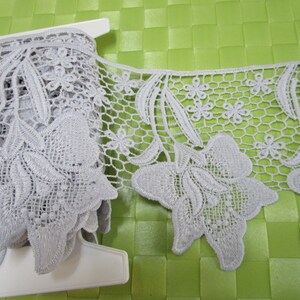 May include: Grey lace trim featuring a floral design. The lace has a delicate, intricate pattern with small flowers and leaves.