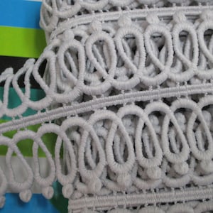 May include: Grey crocheted trim featuring a repeating pattern of loops and small balls. The trim is soft and delicate, and would be ideal for adding a touch of elegance to any project.