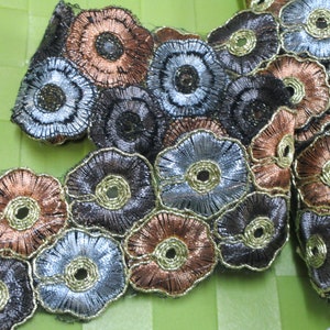 May include: A close-up of a decorative trim featuring a repeating pattern of silver, gold, and brown flowers. The trim is made of a delicate, lace-like material.