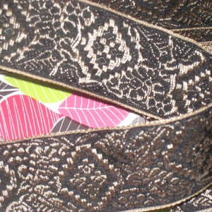 May include: Black and gold trim with a floral pattern. The trim is woven and has a raised texture.