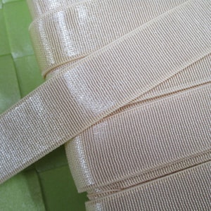 May include: A close-up of ivory-colored, shimmery ribbon with a ribbed texture. The ribbon is folded and layered, showing the texture and sheen.