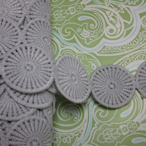 May include: Grey crocheted trim with a circular design. The trim is made of a soft, delicate material and features a repeating pattern of circles with a raised centre.
