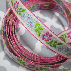 Puede incluir: Cinta blanca con borde rosa y un patrón repetido de flores rosas, azules y verdes.