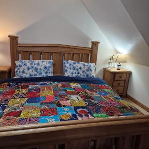 May include: A wooden bed frame with a blue and white patterned quilt. The quilt is made of many different fabrics sewn together in a patchwork design. The bed has a headboard and footboard, and there are two pillows on the bed.