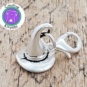May include: Silver charm in the shape of a witch's hat with a pointed top and a wide brim. The charm has a silver clasp for attaching to a bracelet or necklace.