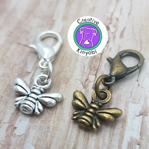 以下が含まれることがあります： 銀とブロンズの仕上げを施した、蜂の形をした2つの編み物マーカー。マーカーはロブスタークロークラスプに取り付けられています。
