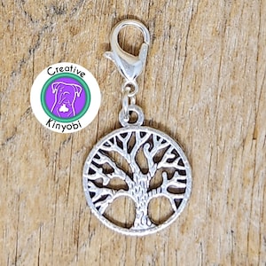 May include: Silver tree of life charm with a silver lobster clasp. The charm is attached to a purple and green circle with the text "Creative Kinyobi".