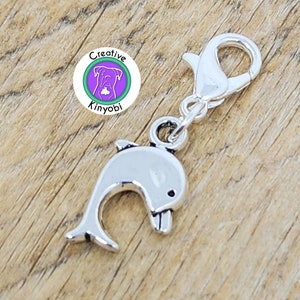 May include: Silver charm with a dolphin design, attached to a silver lobster clasp. The charm is a popular addition to necklaces, bracelets, and keychains.