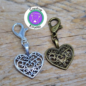 May include: Two silver and bronze heart-shaped charms with intricate filigree designs. Each charm has a lobster clasp attached to a silver and bronze chain.