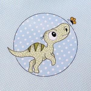 May include: A light blue fabric tote bag with a white polka dot pattern. A cartoon dinosaur with a green and brown body and a butterfly are printed on the bag.
