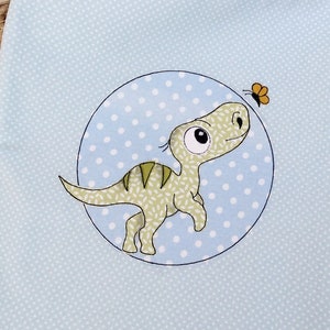 May include: A light blue tote bag with a white polka dot pattern. The bag features a green dinosaur with a butterfly above it.