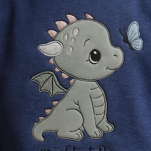 May include: Navy blue sweatshirt featuring an embroidered gray dragon with a butterfly. The dragon has a friendly expression and is detailed with scales and wings. The text "möchtest Du mein Freund sein..." is below the dragon.