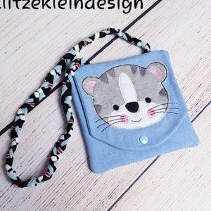 May include: A small blue fabric bag with a grey and white cat face embroidered on the front. The bag has a black and white braided strap.