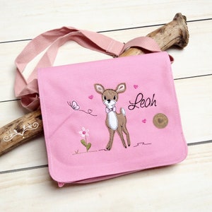 May include: Pink canvas bag with a brown embroidered deer, a pink flower, and a butterfly. The bag has a pink strap and the name "Leah" is embroidered on the front.