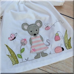 May include: A white baby dress with an embroidered gray mouse wearing a pink and white striped dress. The mouse is surrounded by green grass, pink flowers, and a ladybug.