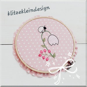Könnte beinhalten: Ein rosa Stoffring mit einem weißen Herzmuster und gestickten Blumen, einer Biene und dem Text "klitzekleindesign".