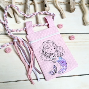 May include: Pink fabric zippered pouch with a pink and white braided strap. The pouch features a smiling mermaid with a purple tail and pink and white polka dots.
