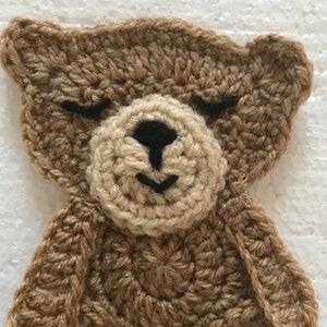 May include: A brown crocheted bear with a beige face and black eyes. The bear has a simple design and is made with a soft yarn.