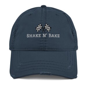 May include: A distressed blue baseball cap with a white embroidered checkered flag design and the text "SHAKE N' BAKE".