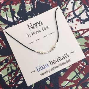 Puede incluir: Un collar de cordón negro con cuentas plateadas que deletrean "Nana" en código Morse. El collar se muestra en una tarjeta blanca con el texto "Nana en código Morse" y el nombre de la tienda "~blue beckett~ www.etsy.com/shop/BlueBeckett".