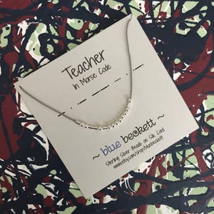 Puede incluir: Una tarjeta gris con el texto "Teacher in Morse Code" y un collar de cuentas de plata. El collar está en un cordón gris y la tarjeta tiene el texto "~ blue beckett ~ Sterling Silver Beads on Silk Cord www.etsy.com/shop/bluebeckett"