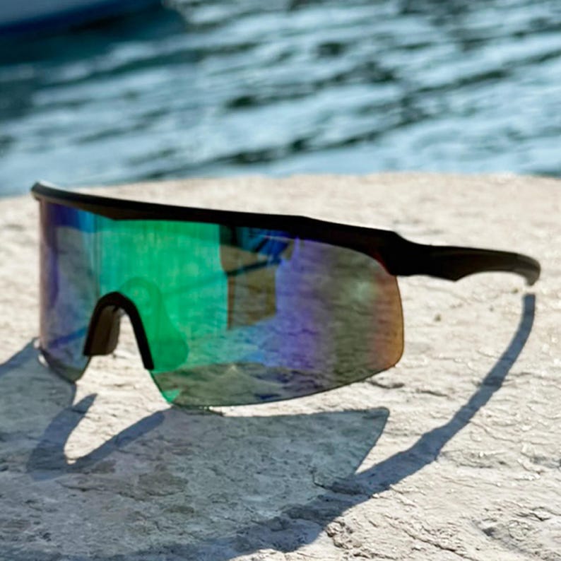 E3 Optics E3-A3 green mirror polarized sunglasses with matte black frame – perfect for boating, fishing, and water sports – angled side view on sunlit dock with water in background.