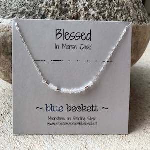 May include: A silver necklace with moonstone beads and a card that reads "Blessed in Morse Code" and "~blue beckett~ Moonstone on Sterling Silver www.etsy.com/shop/bluebeckett"