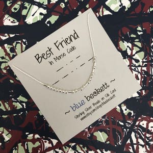 Puede incluir: Una tarjeta blanca con el texto "Best Friend in Morse Code" y un collar de cuentas de plata. La tarjeta también incluye el texto "~ blue beckett ~ Sterling Silver Beads on Silk Cord www.etsy.com/shop/bluebeckett"