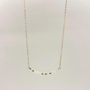 May include: A delicate gold chain necklace with a row of small white beads and gold spacers.