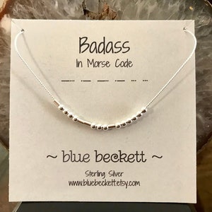 May include: A silver necklace with a message in Morse code that reads "Badass in Morse Code". The necklace is on a white card with the text "~blue beckett~ Sterling Silver www.bluebeckettetsy.com"