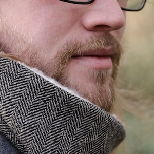 May include: Close-up of a man's face with a beard and a black and white patterned scarf around his neck.
