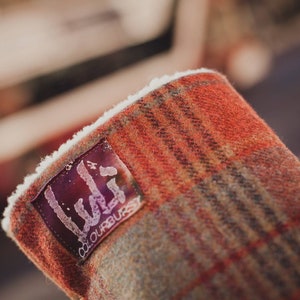 May include: Close-up of a red and brown plaid fabric with a white fleece lining. A black label with the text "Lula" and "colourburst" is attached to the fabric.