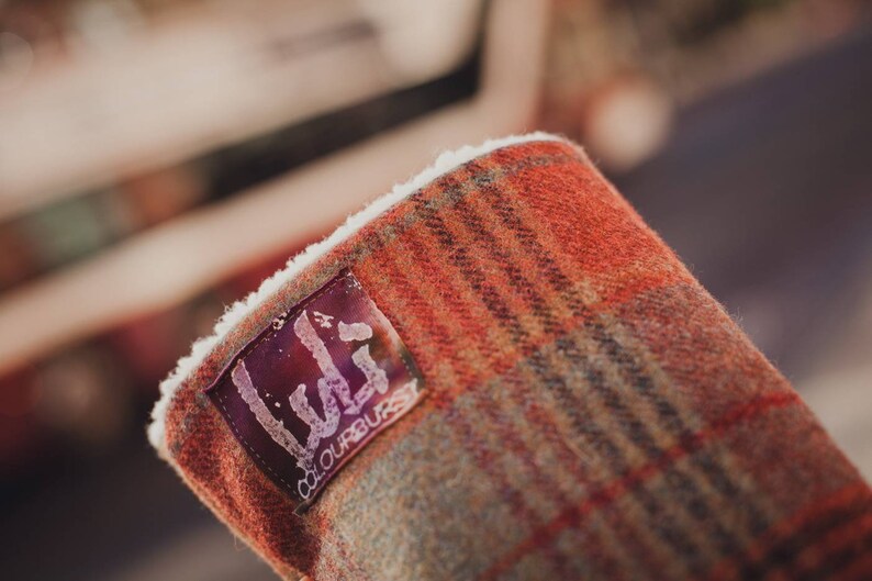 May include: Close-up of a red and brown plaid fabric with a white fleece lining. A black label with the text "Lula" and "colourburst" is attached to the fabric.