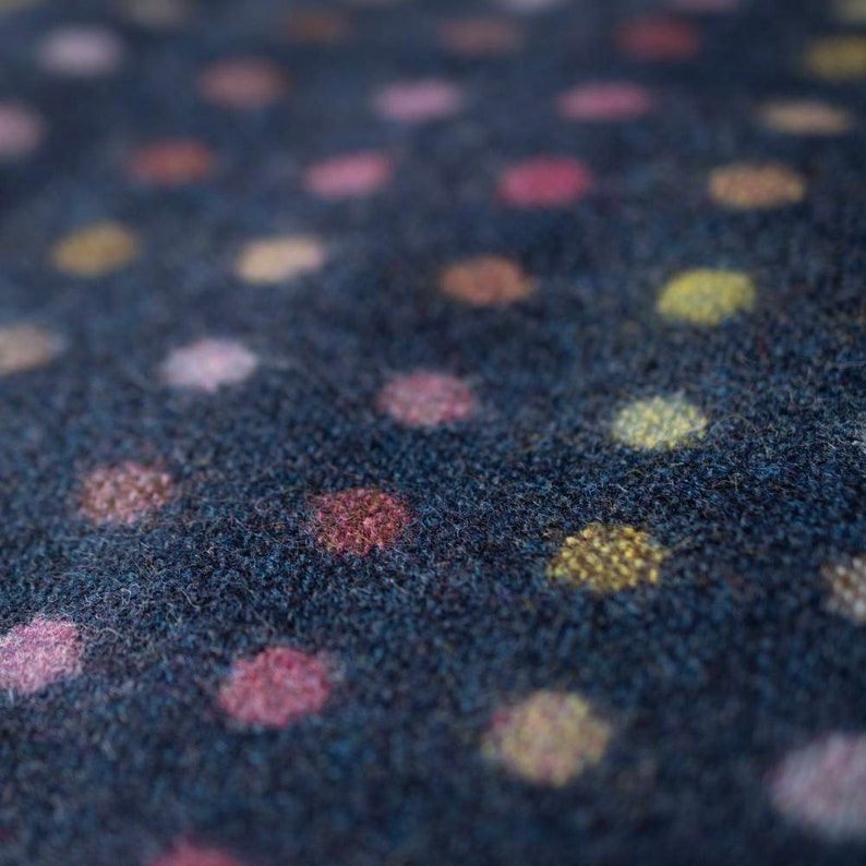 May include: Close-up of a dark blue fabric with a polka dot pattern. The dots are in shades of pink, yellow, and brown.
