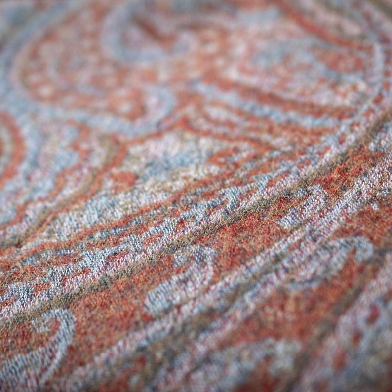 May include: Close-up of a woven fabric with a paisley pattern in shades of red, blue, and brown.