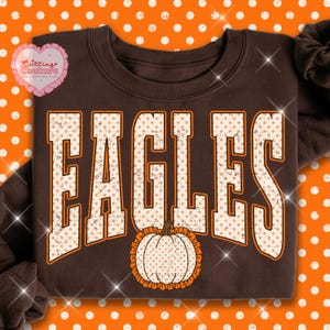 May include: A dark brown crewneck sweatshirt featuring the word EAGLES in large, block-style letters. The letters have a white background with orange polka dots and a distressed texture. A pumpkin graphic with matching polka dots sits below.