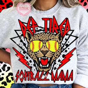 K&ouml;nnte beinhalten: Hellgraues Sweatshirt mit einem Leoparden, der Baseball-Sonnenbrillen tr&auml;gt. Der Text lautet "Def Tired Softball Mama" in Rot, mit roten Blitzakzenten. Ein rosa herzf&ouml;rmiges Logo befindet sich in der oberen linken Ecke.