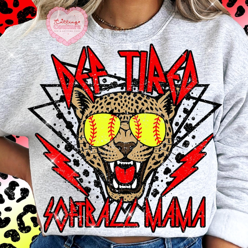 K&ouml;nnte beinhalten: Hellgraues Sweatshirt mit einem Leoparden, der Baseball-Sonnenbrillen tr&auml;gt. Der Text lautet "Def Tired Softball Mama" in Rot, mit roten Blitzakzenten. Ein rosa herzf&ouml;rmiges Logo befindet sich in der oberen linken Ecke.