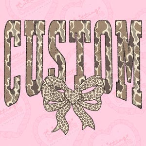 Peut inclure: Sur fond rose, le mot « CUSTOM » est écrit dans une police de style camouflage vieilli. Un nœud léopard est centré en dessous. Le design a une esthétique vintage et champêtre.