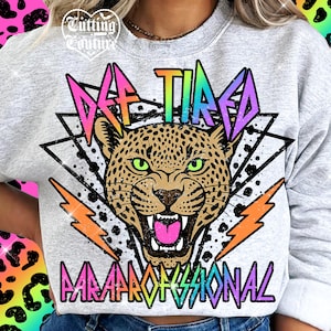May include: A light gray sweatshirt with a leopard graphic and the words "Def Tired Professional" in a colorful, retro font. The leopard has green eyes and an open mouth. Orange and yellow lightning bolts are on either side.
