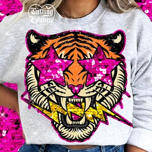May include: A light gray sweatshirt featuring a tiger graphic with pink sequin star-shaped sunglasses and a yellow lightning bolt. The tiger has orange and black stripes. The text "Cutting Couture" is at the top left.