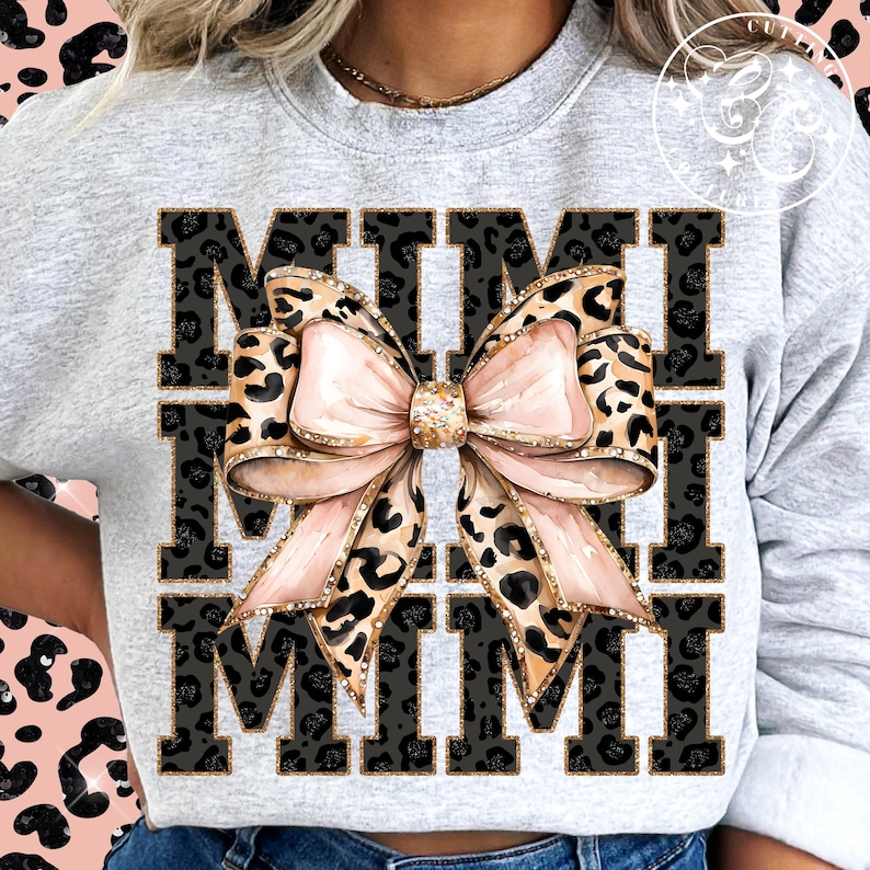 Pu&ograve; includere: Una felpa grigia con la parola "MIMI" stampata in lettere nere con un motivo leopardato. Un grande fiocco rosa con dettagli di glitter dorati &egrave; centrato tra le due parole.
