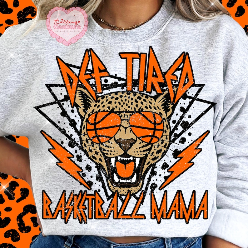 May include: A light grey sweatshirt with a graphic design featuring a leopard wearing basketball sunglasses. The text reads "Off Tired Basketball Mama" in orange and black.