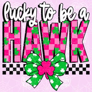 May include: A graphic design with the text "lucky to be a HAWK" in white, over a pink and green checkered pattern. A green bow with white shamrocks and a pink shamrock in the center is at the bottom. The background is light pink.