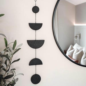 May include: A black and white geometric wall hanging with a chain and five shapes: a circle, two half circles, and two quarter circles.