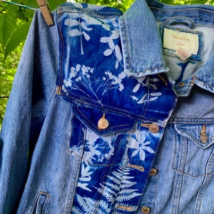 May include: A light blue denim jacket with white floral patterns on the front and sleeves. The jacket has a label that says "FOREVER 21 DENIM".