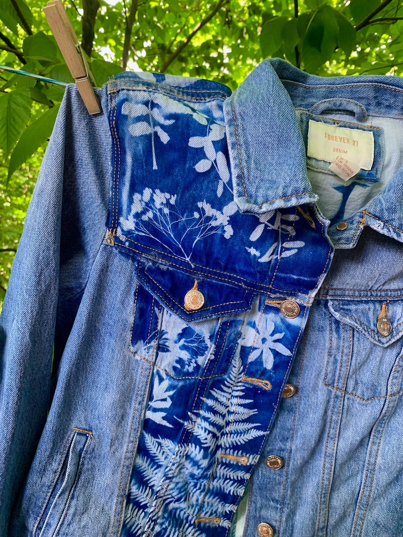 May include: A light blue denim jacket with white floral patterns on the front and sleeves. The jacket has a label that says "FOREVER 21 DENIM".