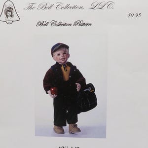May include: A doll pattern for a boy doll named "Nicki" with a red jacket, yellow shirt, black pants, and a blue cap. The doll is holding an apple and a plaid backpack. The pattern includes instructions for making the doll's body, pants, shirt, jacket, and cap. The pattern is from The Bell Collection, LLC.