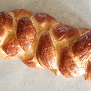 Puede incluir: Una hogaza de pan trenzado con una corteza dorada. El pan est&aacute; horneado a la perfecci&oacute;n y tiene un glaseado brillante.